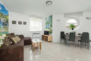 A bright living room with a brown sectional sofa, white walls, and a dining table with four black chairs in the background.