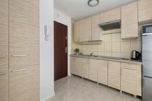 A kitchen with wood-textured cabinets, a silver refrigerator, and tiled walls next to a dark wooden entrance door.