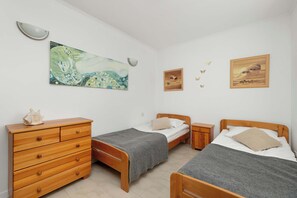 A bedroom with two wooden single beds, orange and grey bedding, and scenic wall art above the headboards.