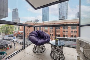 The balcony with a cozy chair and table is the perfect spot for morning coffee with a city skyline view.

