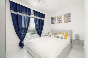 A cozy bedroom with a large bed, white bedding, and dark blue curtains.
