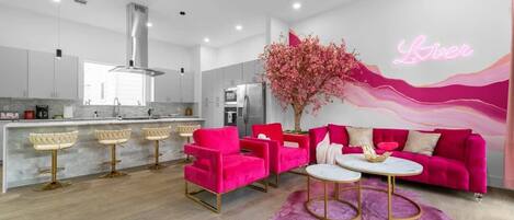 Bright living room w/ bold pink accents, comfy seating, and natural light that makes the space feel fun & welcoming.