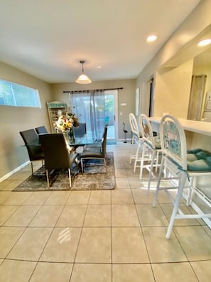 Dining has table, breakfast bar, view to living room, kitchen and opens to pool