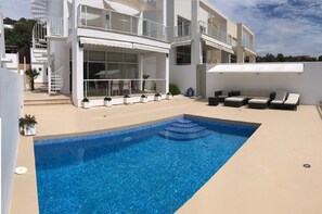Vista frontal de la casa con piscina y muebles de terraza.
