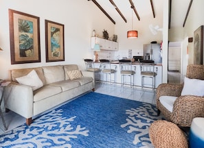 Kas di Amor's cozy living room boasts coastal decor, a sleeper sofa, a banana chair, swivel stools, and stunning ocean views.