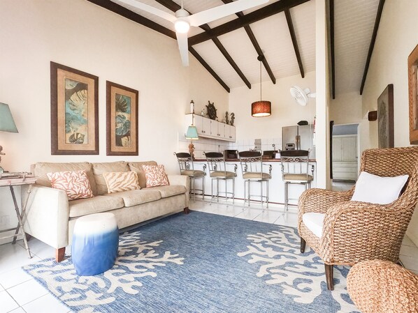 Kas di Amor's cozy living room boasts coastal decor, a sleeper sofa, a banana chair, swivel stools, and stunning ocean views.