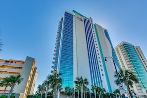 Modern high-rise building with sleek glass panels and palm trees.