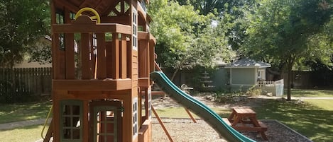 Private playground in backyard with swings, slide, clubhouse and picnic table