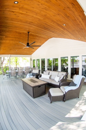 Large covered back porch with couches loungers,  a large table and tv