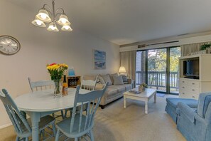 The living room is adorned with a balcony, a smart TV, and a dining table for four. Adding to the comfort, there is a single sofa accompanied by a footrest.