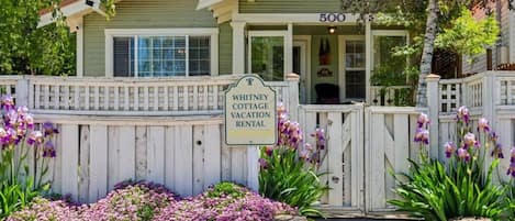 A picturesque entrance with blooming flowers, birch trees, and a copper roof.