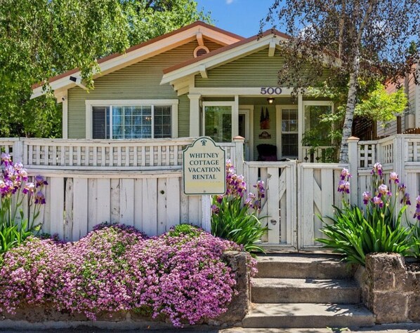 A picturesque entrance with blooming flowers, birch trees, and a copper roof.