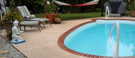 Many seating areas around the blue glistening pool, including gas grill.