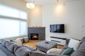 Living room w/ gas fireplace, flatscreen TV, DVR, soundbar and large sectional.