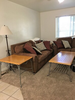 The living room has a sofa, love seat, side tables, TV, games and books.
