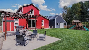 Fenced backyard with cement patio, BBQ, picnic tables and seating, playground