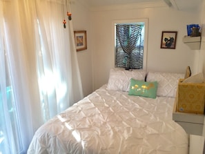 Bright sunlit bedroom with Queen bed, ceiling fan, heat or A/C.