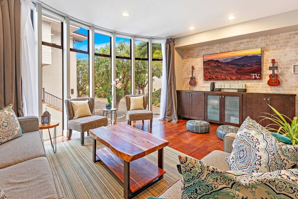Step into a beautifully decorated living room bathed in natural light, thanks to stunning floor-to-ceiling windows that frame breathtaking views of Maui’s lush landscape.