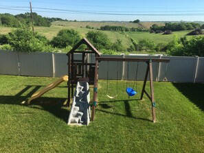 Kids play set inside fully fenced yard. 