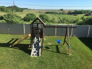 Kids play set inside fully fenced yard.