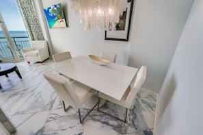 - Sleek dining space with ocean views, perfect for enjoying meals or gathering with loved ones - Modern white décor & a statement chandelier create an inviting coastal atmosphere - Dine in style with a bright, airy setting just steps from the balcony