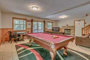The game room complete with a pool table, couches, a TV, fireplace, and table with chairs.