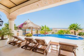 Covered patio lounge chairs and pool with ocean view