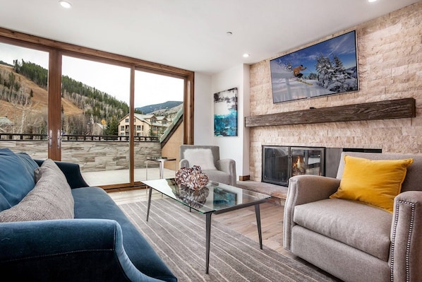 Modern living room with flat screen TV, wood burning fireplace and mountain views.