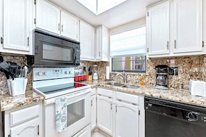 Modern kitchen with sleek white cabinetry, granite countertops, and full amenities.
