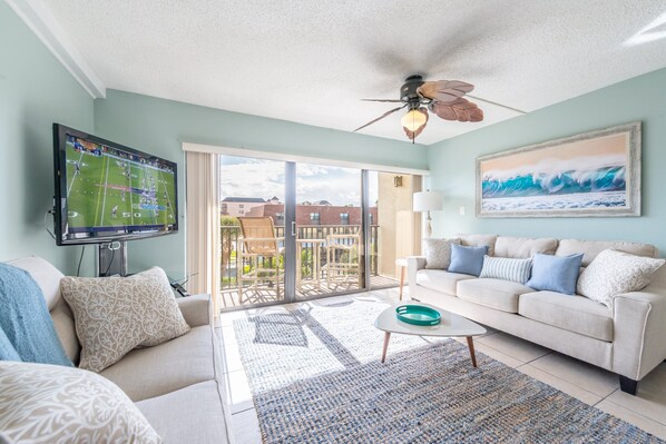 Bright and airy living room with a large TV and direct balcony access.