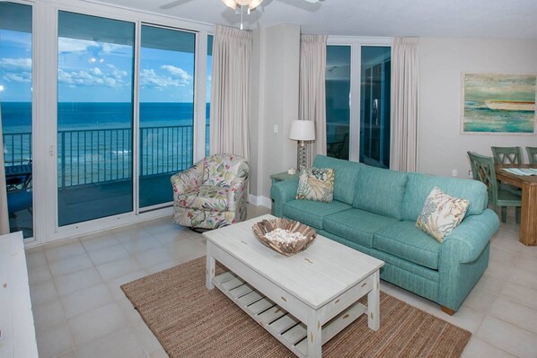 Tiled living room with sofa, chair, coffee table, ceiling fan and sliding glass door to balcony overlooking Gulf