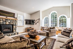 Tall windows and rock fireplace and cozy furniture invite comfort in this gorgeous living room