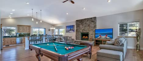 Step into luxury in this upstairs great room with full pool table, gas fireplace adorned in stone, large HDTV, and open layout to the kitchen and dining area