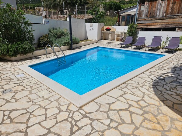 Pool with outdoor shower and loungers.  Outdoor electric grill and stone sink.