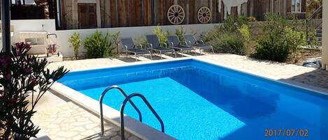 Pool and loungers with backdrop of olive groves and hills.