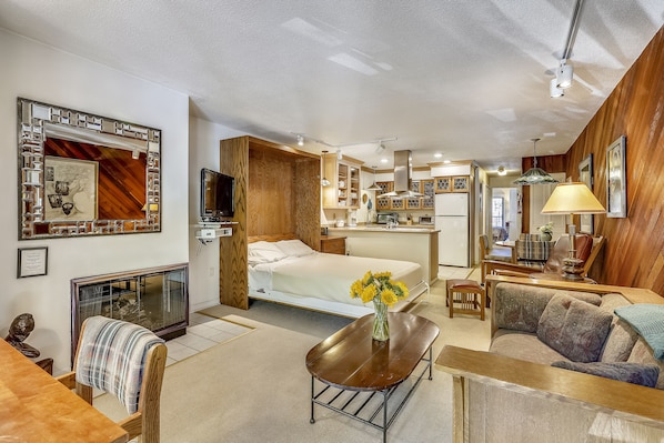 View from front entry over living room, queen Murphy bed, kitchen, eating area and hallway leading you to the bedroom with private deck.