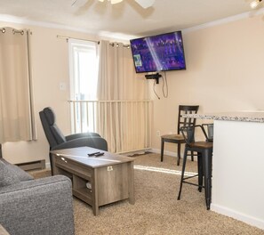 Comfortable living area featuring a sleeper sofa, sofa chair, small coffee table, TV and kitchen island for meal prep and socializing.