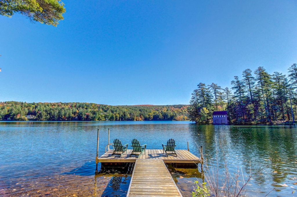 A long dock with three chairs at the end sits on a lake under clear blue skies at one of the most popular waterfront Vermont vacation rentals