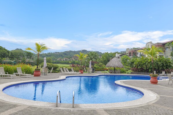 A vibrant community pool area featuring tables and seating for outdoor dining, a dedicated BBQ area for grilling, and a relaxing jacuzzi.