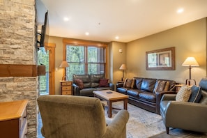 Living area featuring cozy furnishings, a mounted TV, balcony access and gas fireplace with beautiful stone surround.