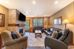 Living area featuring cozy furnishings, a mounted TV, balcony access and gas fireplace with beautiful stone surround.