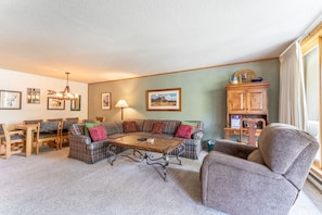 Spacious living area with cozy furniture, wood-burning fireplace, flat screen TV and balcony access.