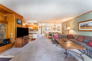 Spacious living area with cozy furniture, wood-burning fireplace, flat screen TV and balcony access.