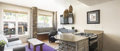 Kitchen breakfast bar and oven/range with granite countertops, living room in the background with bright purple area rug for a beautiful pop of color