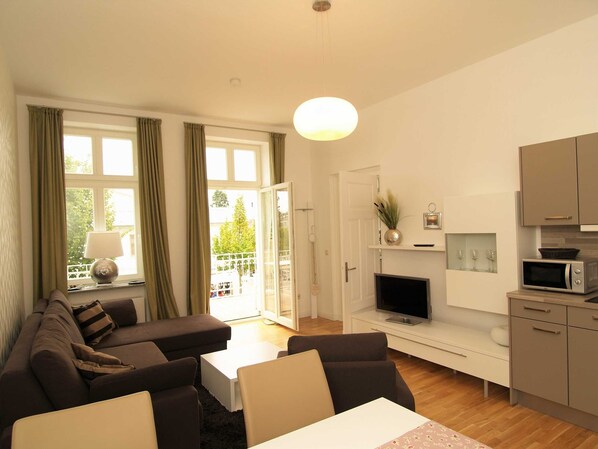 Das Wohnzimmer mit gemütlicher Couchgarnitur und TV sowie einer Essecke und Zugang zum Balkon