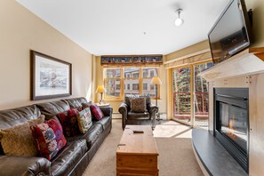 Living area with a flat-screen TV mounted above the gas fireplace, cozy furniture, and access to the private balcony.