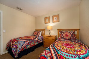 Colorful bedroom with two beds, a dresser, and bright wall art.