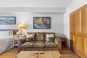 Living area with sleeper sofa, mounted flat screen TV and hardwood flooring.