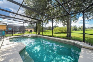 Pool showing screen enclosure and spa overlooking wide grassy area
