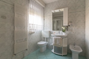 A modern bathroom with a glass shower stall, washbasin, toilet and bidet.